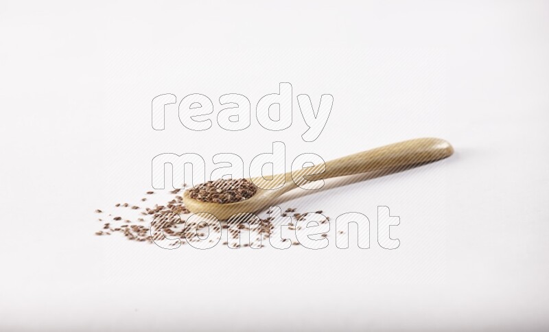 A wooden spoon full of flax seeds on a white flooring