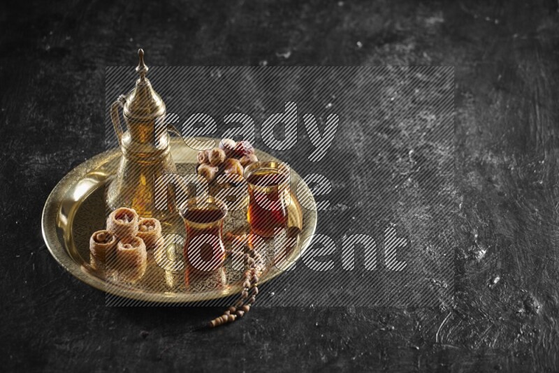 Oriental sweets with dates and a drink on a metal tray in a dark setup