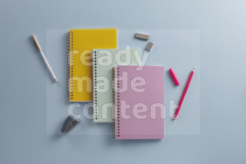 Multicolored notebooks with different school supplies on blue background