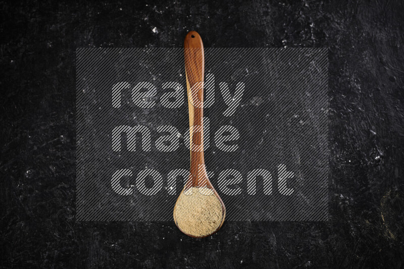 A wooden ladle full of ground ginger powder on black background
