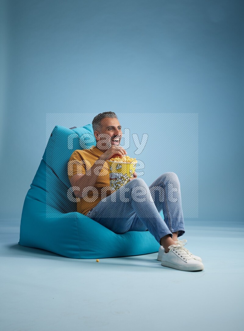 A man sitting on a blue beanbag and eating popcorn