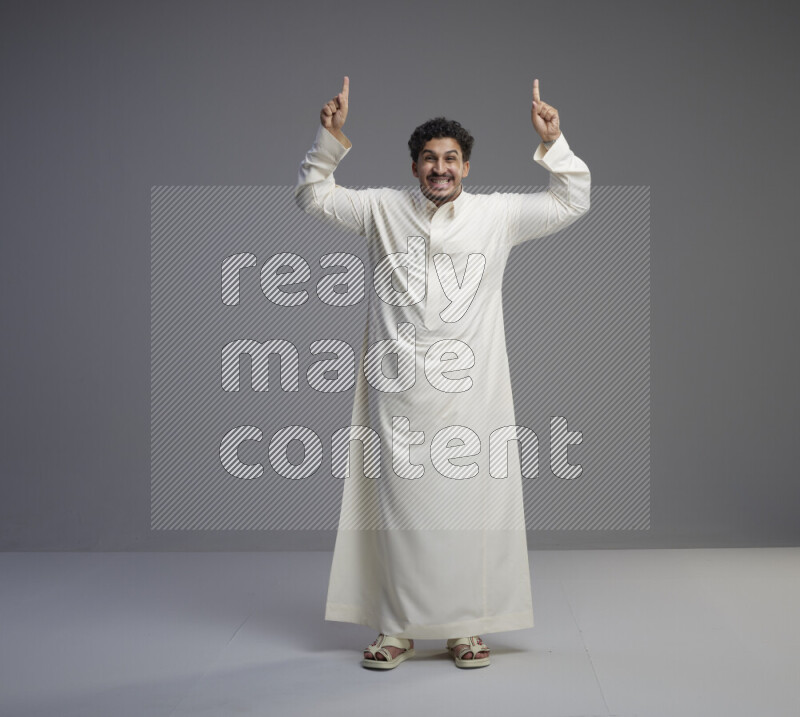 A Saudi man standing wearing thob interacting with the camera on gray background