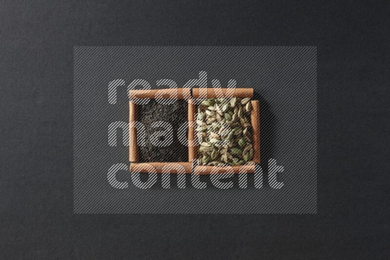 مربعان من أعواد القرفة ممتلئان بحبوب الهيل والشاي الأسود علي خلفية سوداء