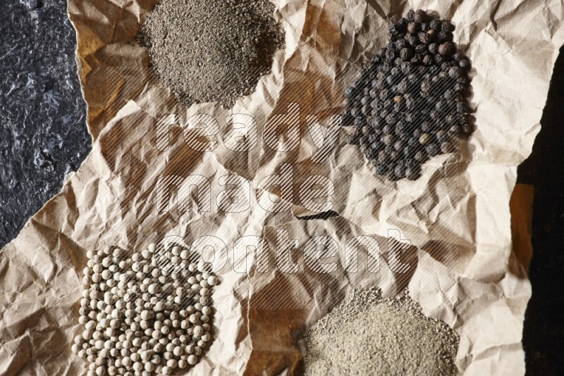 Crumpled pieces of paper full of black and white pepper beads and powder on a textured black flooring
