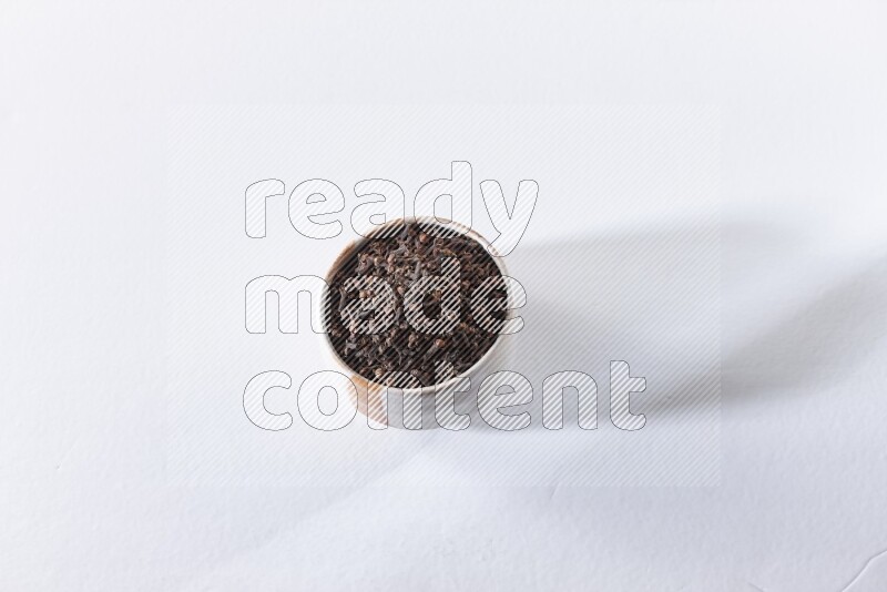 A beige ceramic bowl full of cloves on a white flooring