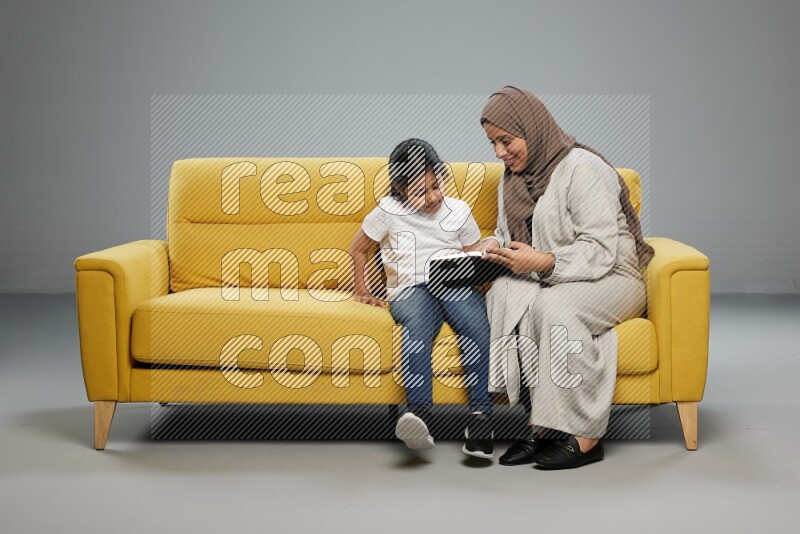 Mom and daughter sitting reading a book on gray background