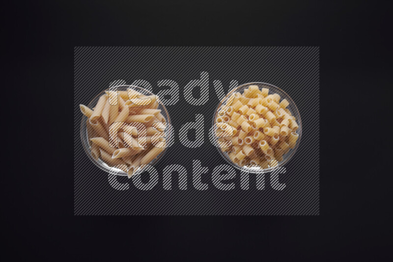 Different pasta types in glass bowls on black background