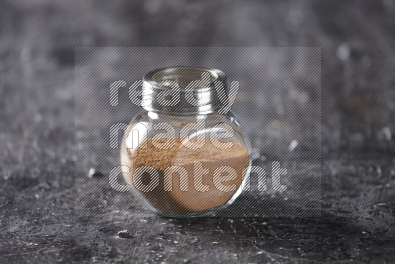 Herbal glass jar full of cinnamon powder on a textured black background