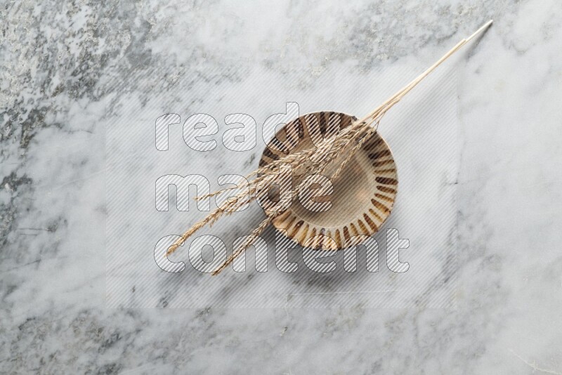 Wheat stalks on multicolored pottery plate on grey marble background