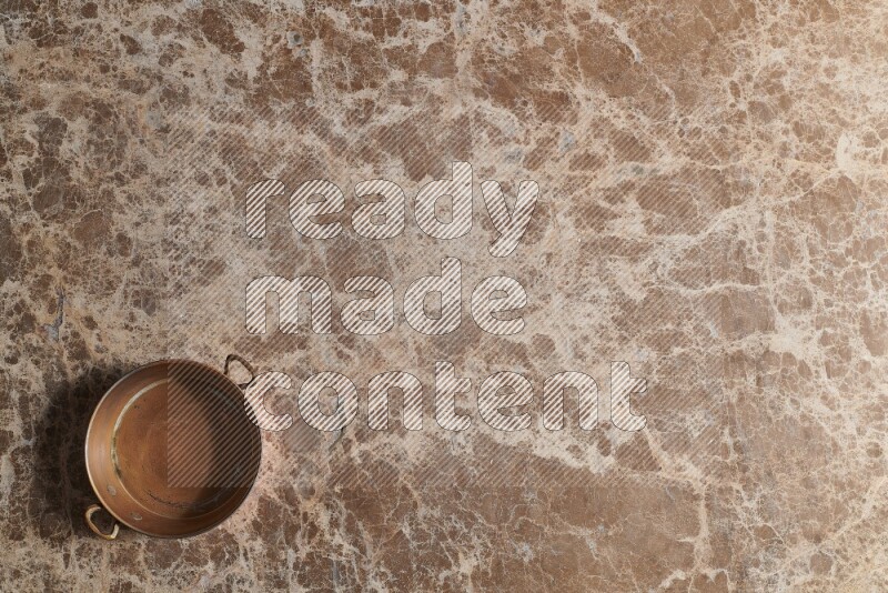 A small copper pan on beige marble background