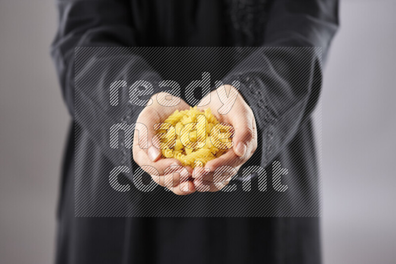 Woman in abaya holding different kinds of pasta in different positions