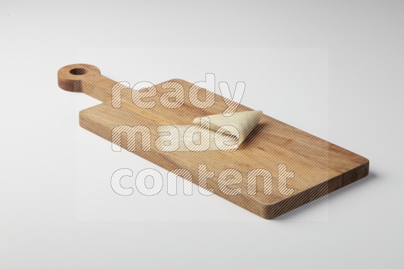 One uncooked samosa on a wooden cutter on a white background