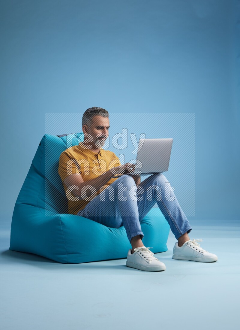 A man sitting on a blue beanbag and working on laptop