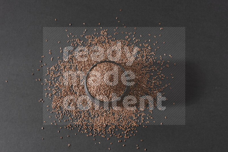 وعاء فخاري أسود ممتلئ بحبوب بذر الكتان محاط بالبذور على أرضية سوداء