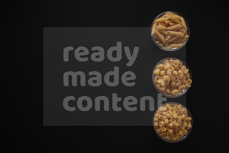 Different pasta types in 3 glass bowls on black background