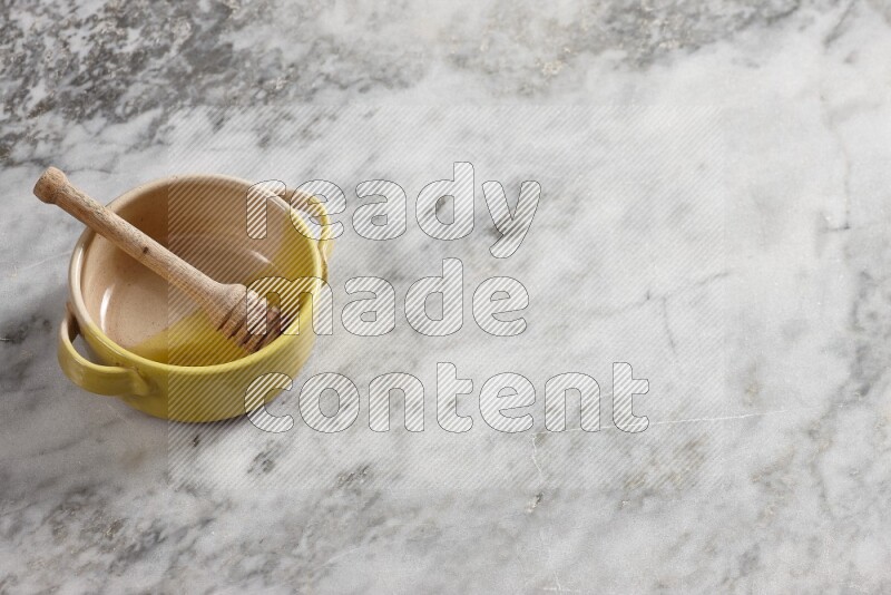 Multicolored pottery bowl with wooden honey dipper in it on grey marble background