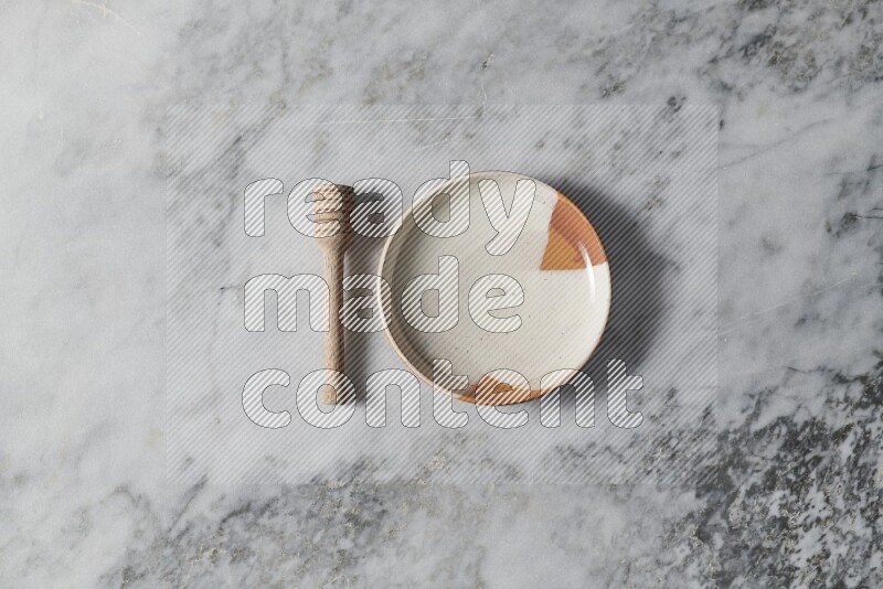 Multicolored pottery plate with wooden honey dipper on the side on grey marble background