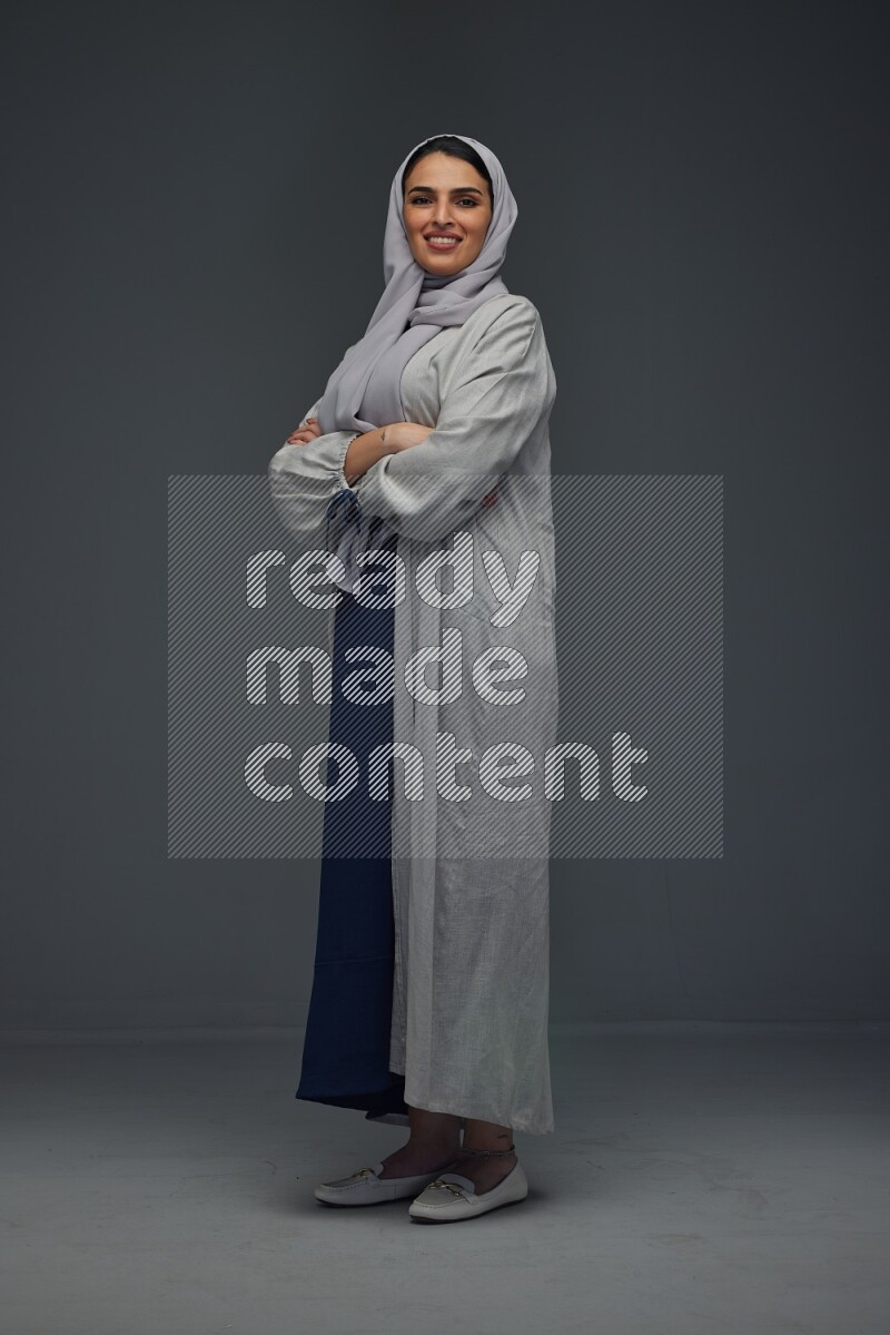 A Saudi woman wearing a light gray Abaya and head scarf standing and making multi poses eye level on a grey background