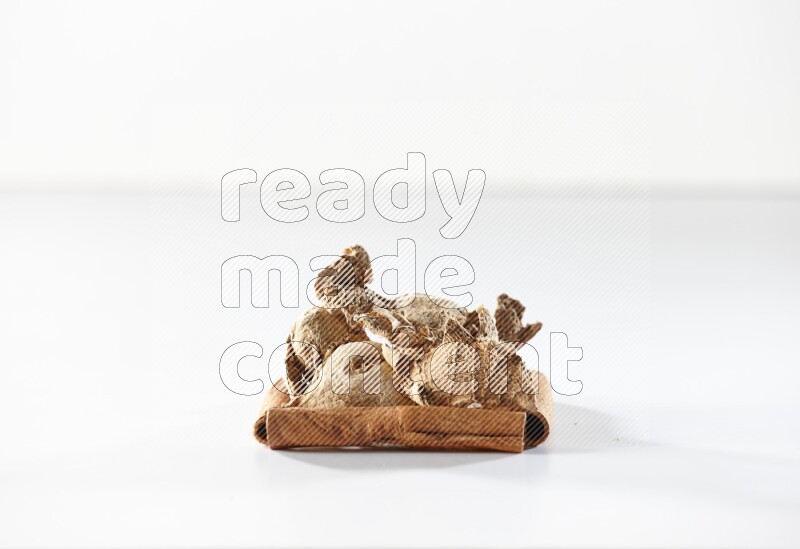 أربعة من أعواد القرفة مكونة شكل مربع بداخلها زنجبيل مجفف علي خلفية بيضاء