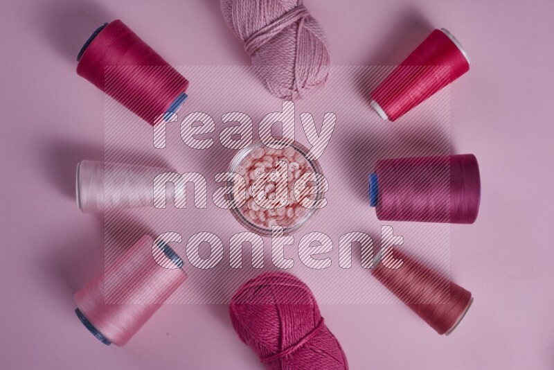 A pink collection of sewing and tailoring tools arranged on a pink background