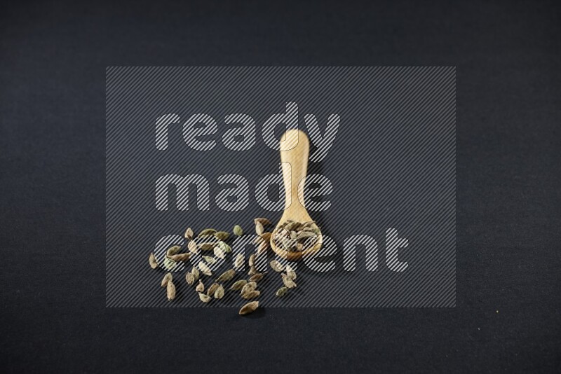 ملعقة خشبية ممتلئة بالهيل على خلفية سوداء