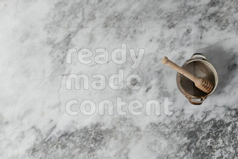 Multicolored pottery bowl with wooden honey dipper in it on grey marble background