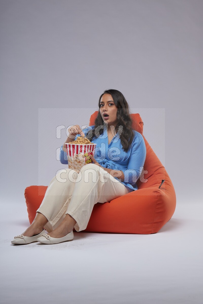 A woman sitting on an orange beanbag and eating popcorn