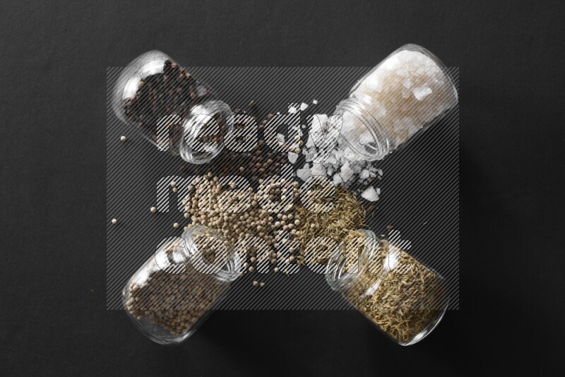 4 glass spice jars full of salt, black peppers, white peppers and cumin on black flooring