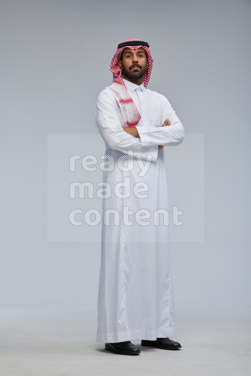 Saudi man Wearing Thob and shomag standing with crossed arms on Gray background
