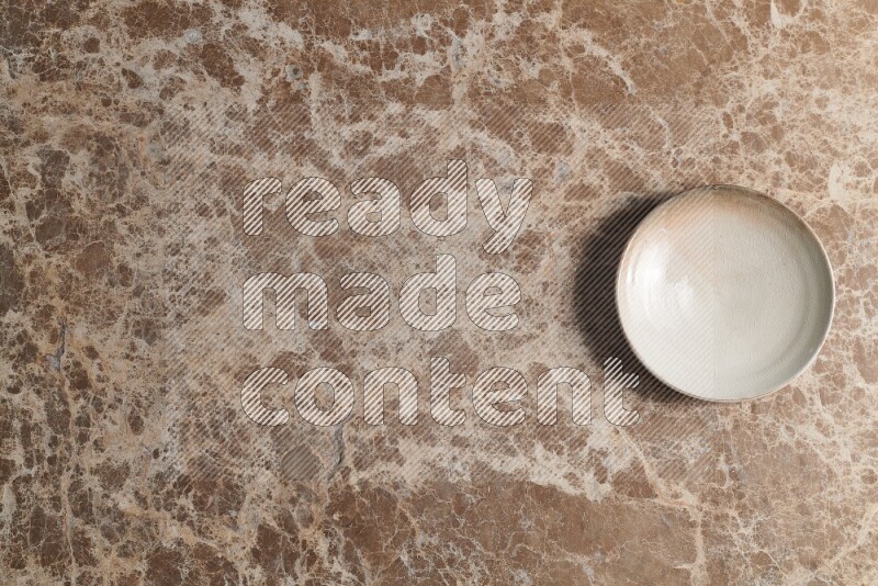 A beige pottery plate on beige marble background