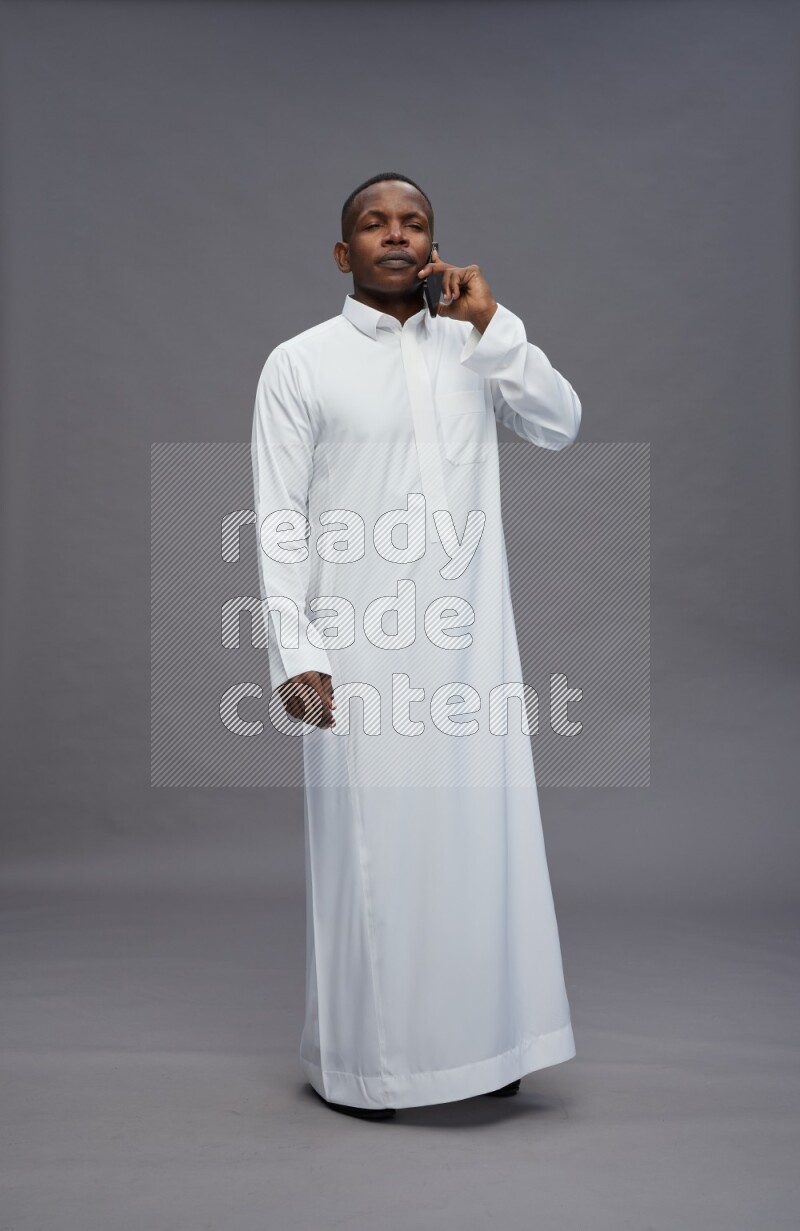 Saudi man wearing thob standing talking on phone on gray background