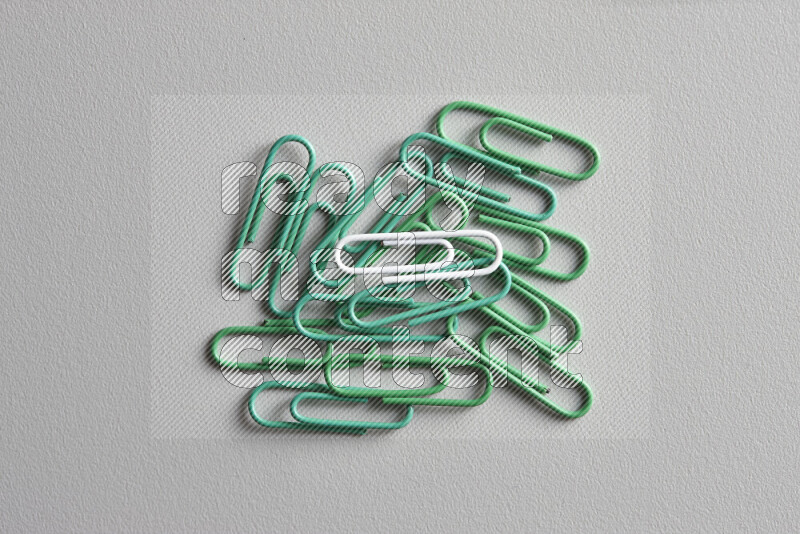 A bunch of green paper clips with a different colored paper clip in the center on grey background