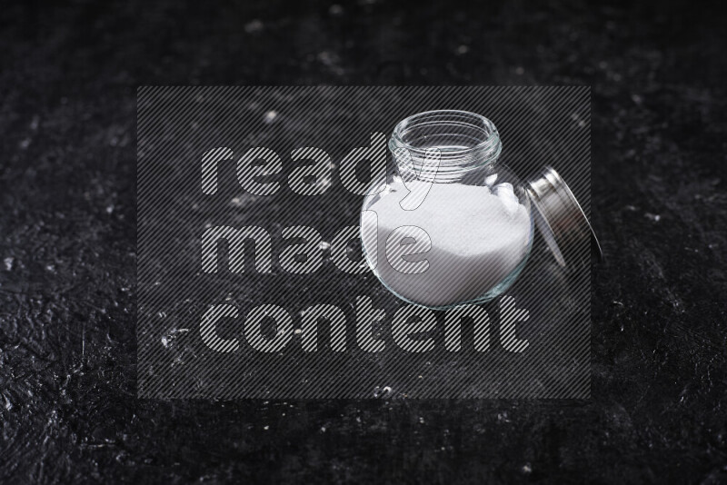 A glass jar full of fine table salt on black background