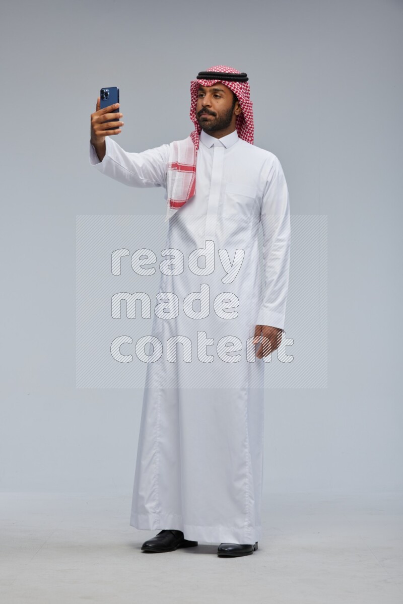 Saudi man Wearing Thob and shomag standing taking selfie on Gray background