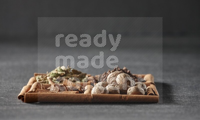 4 مربعات من عيدان القرفة ممتلئة بقطع القرفة وحبوب الهيل والقرنفل وجوزة الطيب على أرضية سوداء