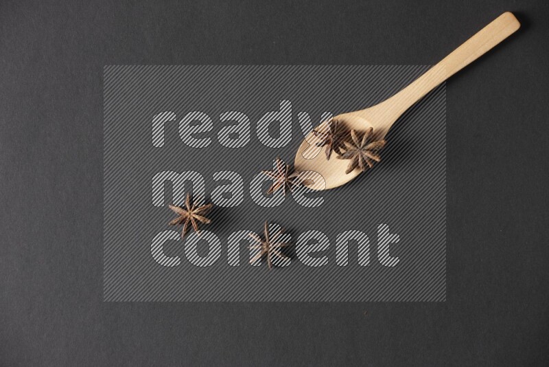 Star Anise in a wooden spoon on more stars anise filling the frame on black flooring