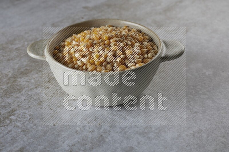 corn kernel in a off-white handheld ceramic bowl on a grey textured countertop