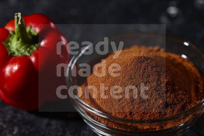 A glass bowl full of ground paprika powder on black background