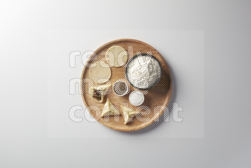 two closed sambosas and one open sambosa filled with meat while flour, salt, and black pepper aside in a wooden dish on a white background