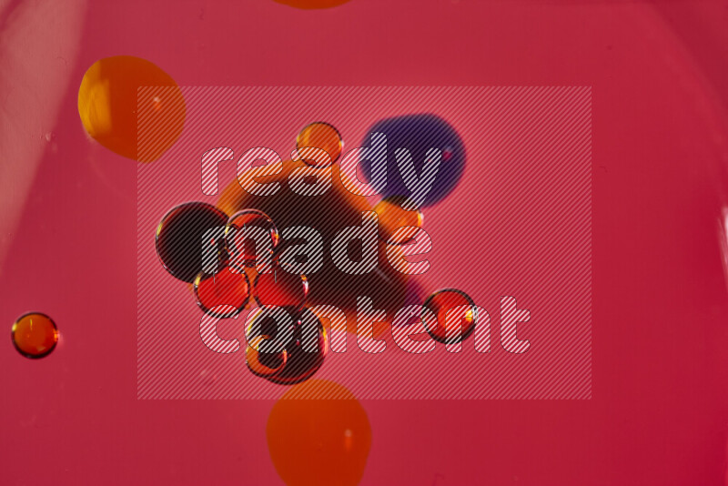 لقطات مقربة لقطرات ألوان مائية حمراء وزرقاء وصفراء على سطح الزيت على خلفية حمراء