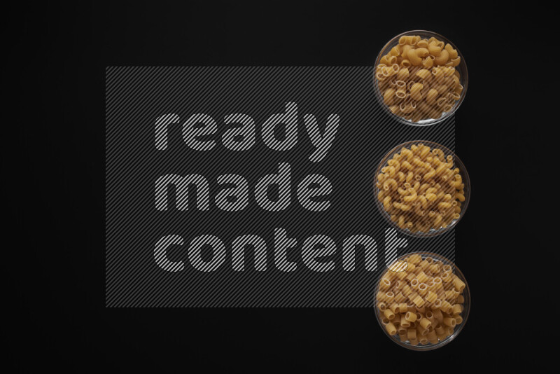 Different pasta types in 3 glass bowls on black background