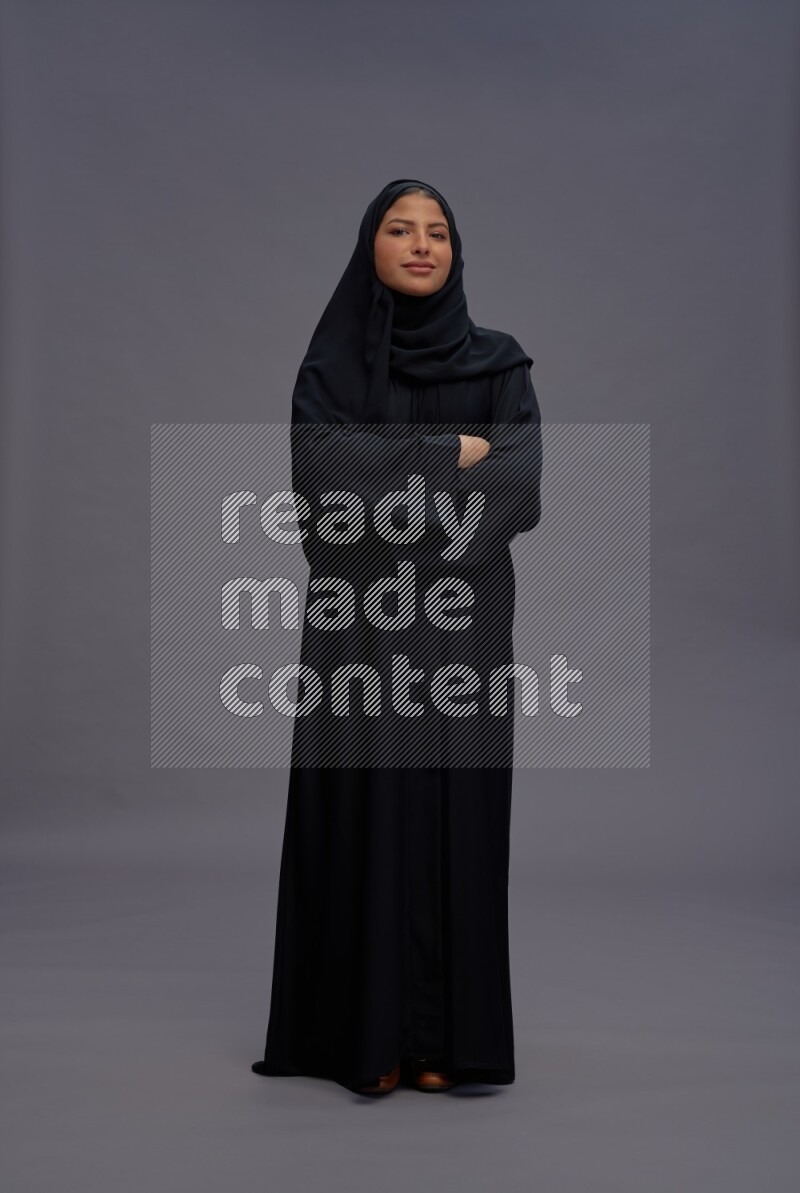 Saudi woman wearing Abaya standing with crossed arms on gray background