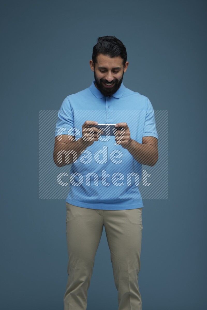 Man playing a game on his phone in a blue background wearing a Blue shirt