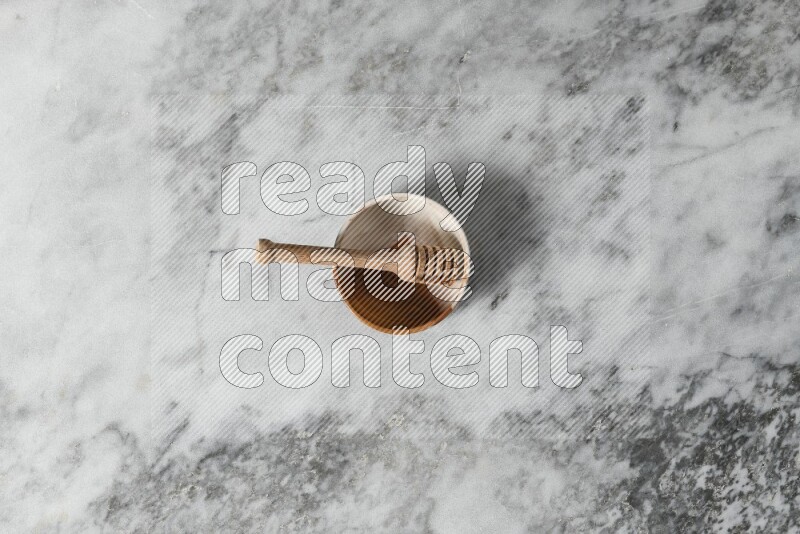 Multicolored pottery bowl with wooden honey dipper in it on grey marble background