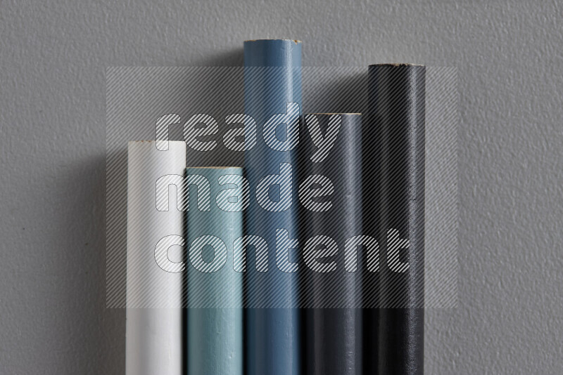 A collection of colored pencils arranged showcasing a gradient of white, grey and black hues on grey background