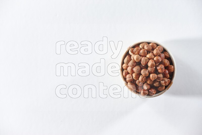 A beige ceramic bowl full of peeled hazelnuts on a white background in different angles