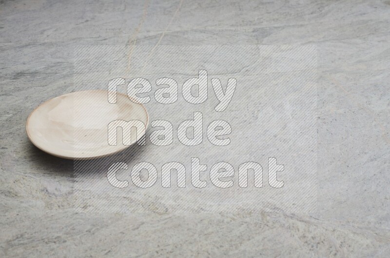 A beige pottery plate on grey marble background