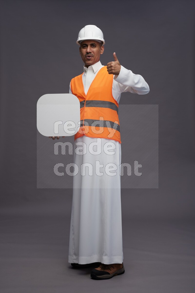 Saudi man wearing thob with engineer vest standing holding social media sign on gray background