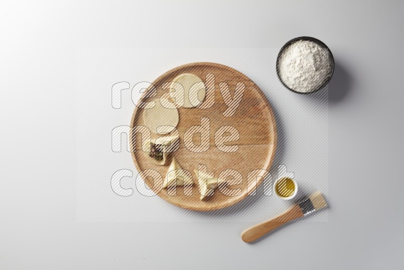 two closed sambosas and one open sambosa filled with meat while flour, and oil with oil brush aside in a wooden dish on a white background