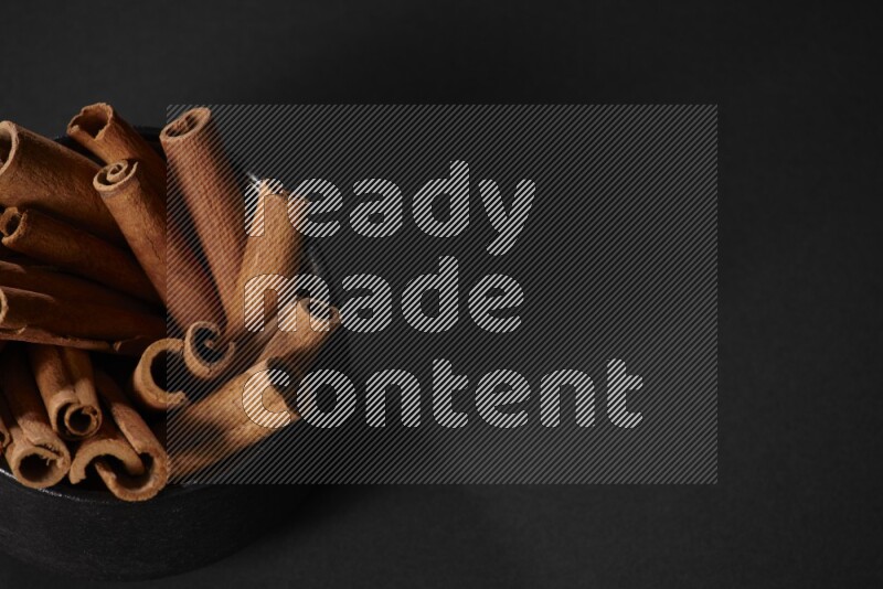 Cinnamon sticks in a black bowl on a black background in different angles